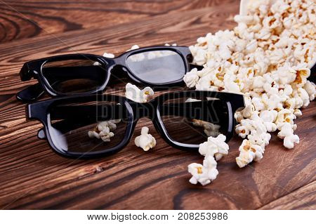 Bowl with scattered popcorn and 3D glasses on a wooden background