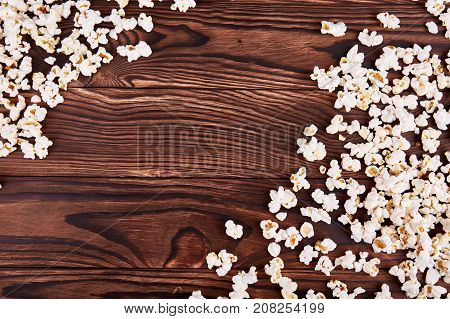 Spilled on the edges of popcorn on a wooden brown background which is sold in the cinema