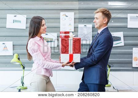 Young happy employees are standing with gifts in the office. They look at each other. Close-up.