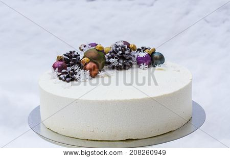 A cake for a Christmas holiday or a new year. A cake with chocolate cones and Christmas-tree toys is made of chocolate. Cake on snow background
