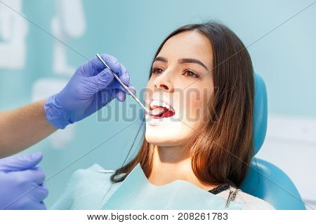 A dentist in purple gloves examines the teeth of a young pretty black-haired girl at his reception