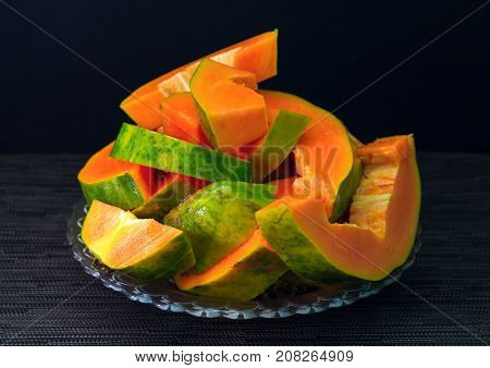 Papaya cut on black background. Cut papaya on plate served for vegetarian breakfast. Healthy and sweet tropical fruit. Exotic fruit with juicy orange flesh and green skin. Fresh papaya juice cooking