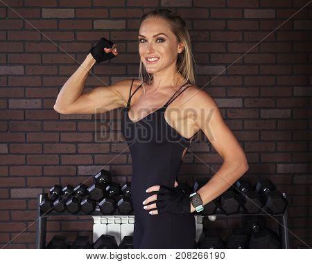 Woman bodybuilder showing the biceps against brick wall in the gym