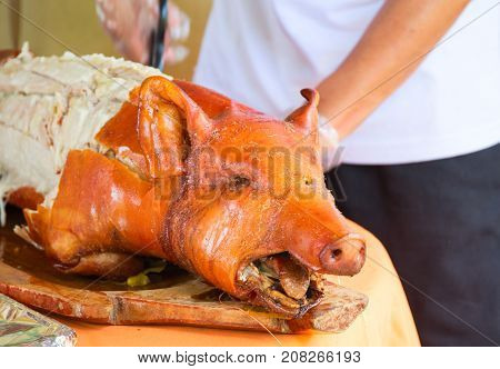Fried pork on table. Waiter cut whole pork. Traditional dish whole roasted pig with head. Delicious meat barbecue. Roasted pork for serving. Fresh juicy pork meat for lunch. Spanish jamon