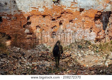 Man in camouflage with a backpack is walking along ruins of city. Post apocalyptic concept
