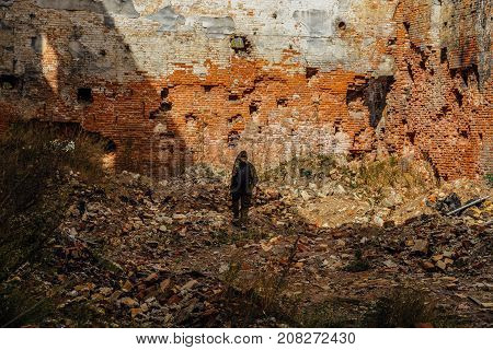 Man in camouflage with a backpack is walking along ruins of city. Post apocalyptic concept
