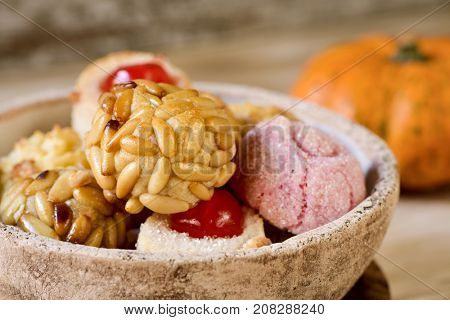 closeup of a rustic bowl with some panellets, typical confection eaten in All Saints Day in Catalonia, Spain, on a wooden table, and a pumpkin in the background