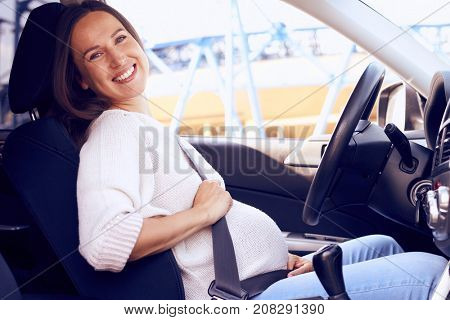 Side view of joyful pregnant woman posing on driver seat in car 