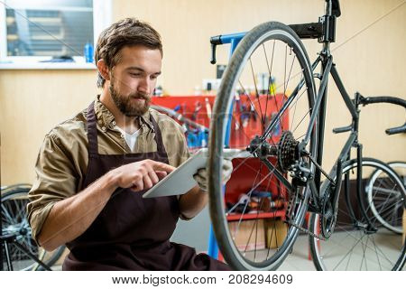 Contemporary repairman with tablet searching for necessary details for bicycle wheels in the net
