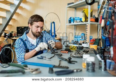 Modern mechanic repairing chain from bicycle wheel by his workplace