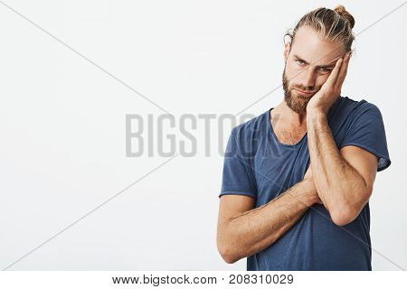 Portrait of hadsome young man with stylish hairstyle and beard in blue t-shirt beig tired after spending day with little kid.
