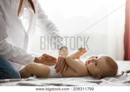 Young mom gentle putting diaper on one years old little son with her tender hands before going out for a walk in park with her husband. Spending special time with family. Family concept.