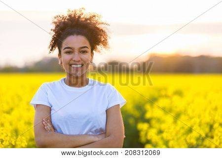 Beautiful mixed race African American girl teenager female young woman happy smiling with perfect teeth at the end of a path in a field of yellow flowers