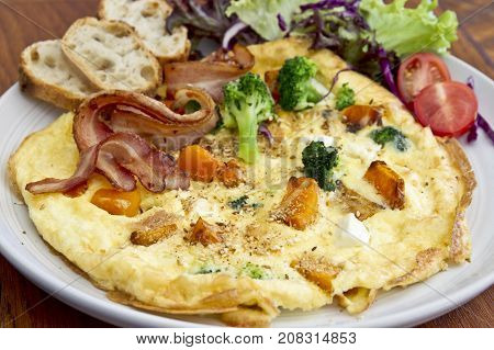 round fritata bread with bacon and vegetables and salad on the side in a white plate