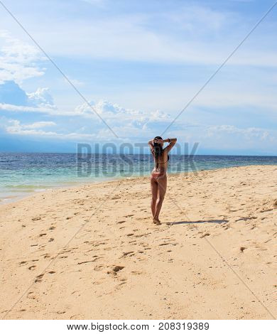 Woman on sunny beach. Tropical beach photo. Beautiful girl on beach. Young woman in bikini under sunshine. Tropical island paradise holiday travel. White sand beach and blue seawater. Sunbathing girl