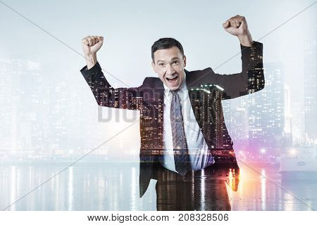 Always winning. Waist up of cheerful businessman standing and keeping his fists raised up while expressing endless happiness