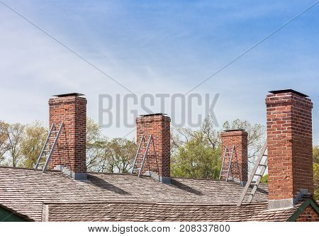 four brick chimneys with individual metal ladders on the roof and cloudy blue sky and trees