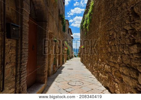 Pienza, Italy - May 27, 2017: Beautiful narrow street with sunlight and flowers in the small magical and old village of Pienza, Val D'Orcia Tuscany.