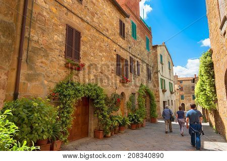 Pienza, Italy - May 27, 2017: Beautiful narrow street with sunlight and flowers in the small magical and old village of Pienza, Val D'Orcia Tuscany.
