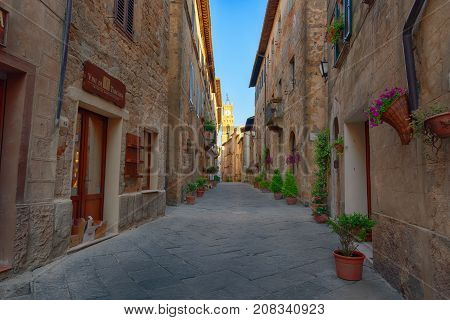 Pienza, Italy - May 27, 2017: Beautiful narrow street with sunlight and flowers in the small magical and old village of Pienza, Val D'Orcia Tuscany.