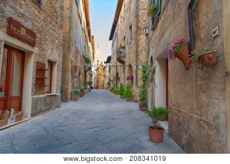 Pienza, Italy - May 27, 2017: Beautiful narrow street with sunlight and flowers in the small magical and old village of Pienza, Val D'Orcia Tuscany.