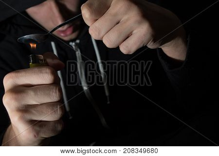The young drug addict prepares heroin with spoon and lighter