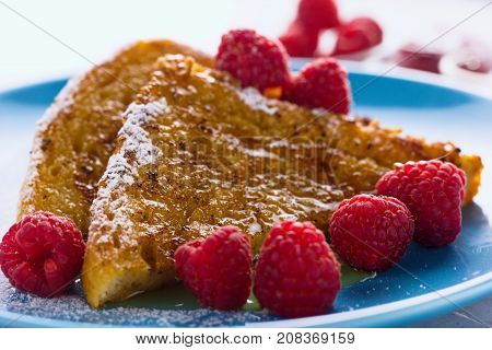 French toast iced with powdered sugar and honey and raspberries