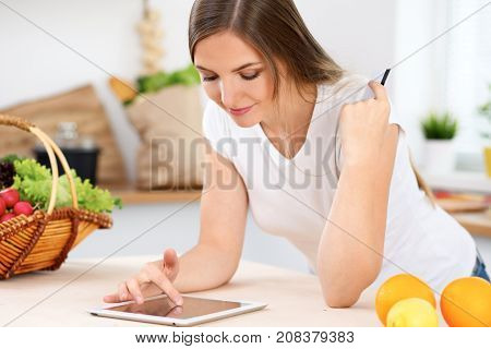 Young woman is making online shopping by tablet computer and credit card. Housewife found new recipe for  cooking in a kitchen