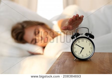 Sleepy young woman stretching hand to ringing alarm willing turn it off. Early wake up, not getting enough sleep, getting work concept