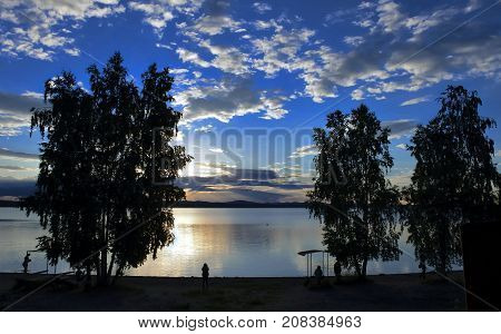 dark silhouettes of trees on the lake shore against the evening cloudy sky, South Ural, Uvildy