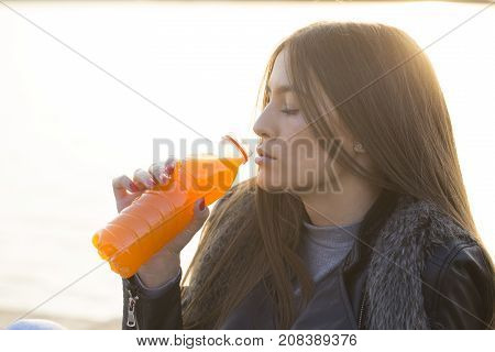 Beautiful young woman sitting outdoors drinking juice and enjoy the beautiful day. lens flare. Selective focus and small depth of field.