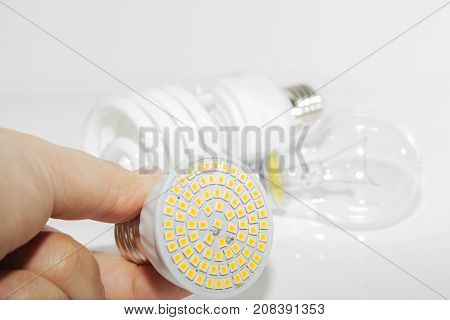 Several different led bulbs and compact fluorescent lamps and the male hand on a light background
