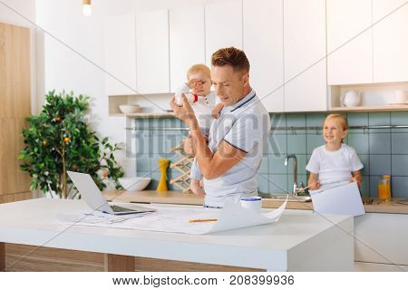 Important project. Pleasant serious smart man holding his baby daughter and looking at the engineering drawing while finishing his project