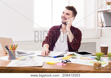 Important call. Young smiling businessman in casual talking on mobile phone in modern white office interior.