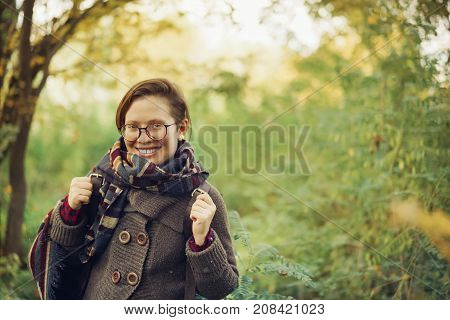 Portrait happy beautiful young girl with glasses and with a big smile in the autumn park. fashion and coziness in autumn.