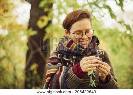 cute happy girl in glasses with a sweatshirt and a scarf found in the forest blueberries and wants to eat it. autumn forest berries and people. focus on blueberries in hands.