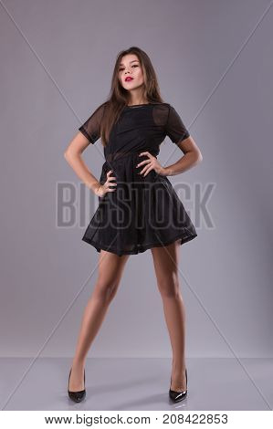 Portrait of a beautiful brunette girl in a little dress red lips and long legs over gray background. Sudio shoot.