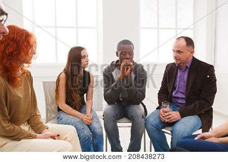 Meeting of support group. Depressed african-american man sitting at rehab group therapy. Psychotherapy, depression, life issues concept