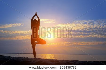 Female silhouette doing yoga asana in slowmotion at sunrise with hands raised to sun