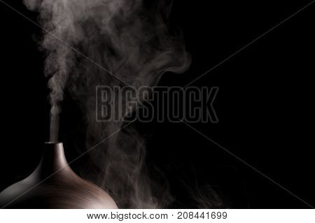 Alternative spa therapy device. Electric essential oil aromatherapy diffuser producing vapor. Close up of atomizer in use against black background.