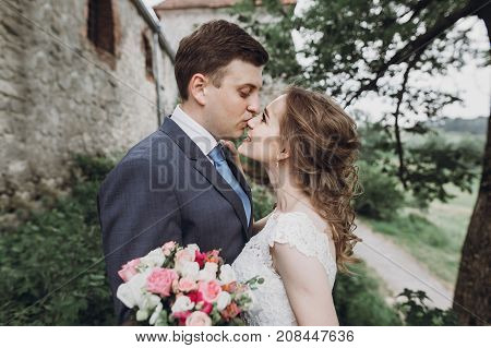 Beautiful Gorgeous Bride And Groom Walking In Sunny Park And Kissing. Happy Wedding Couple Hugging I