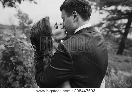 Beautiful Gorgeous Bride And Groom Walking In Sunny Park And Kissing. Happy Wedding Couple Hugging I