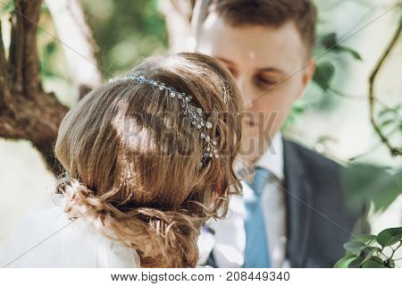 Beautiful Gorgeous Bride And Groom Kissing In Sunny Spring Park Among Green Leaves And Blooming. Hap