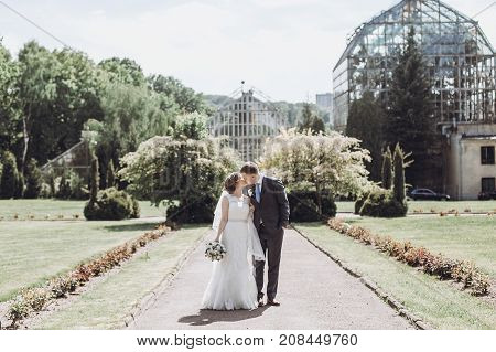 Beautiful Gorgeous Bride And Groom Kissing In Sunny Spring Park And Enjoying Day. Happy Wedding Coup