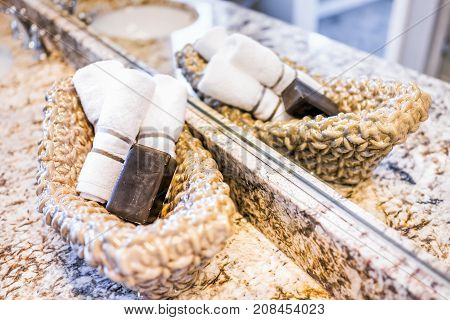 Closeup Of Soap And Hand Towels In Woven Basket In Bathroom Granite Countertop With Sink And Mirror