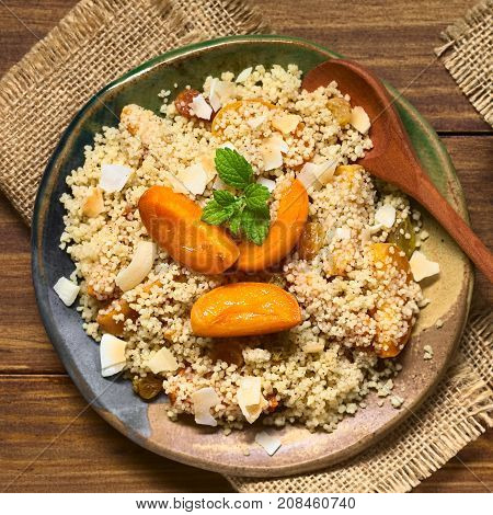 Couscous dessert with apricots yellow raisins coconut flakes and cinnamon garnished with lemon balm leaf photographed overhead with natural light (Selective Focus Focus on the top of the dessert)