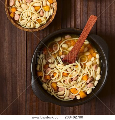 Chilean traditional Porotos con Riendas (beans with reins) dish of cooked dried beans with pumpkin onion spaghetti and sausage in rustic bowls photographed overhead on dark wood with natural light
