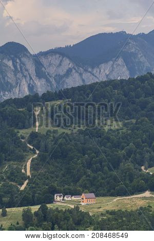Picturesque rural scenery with house and country road uphill in Carpathian mountain, Romania. Countryside view in Transylvania. Mountains and cloudscape in the background.