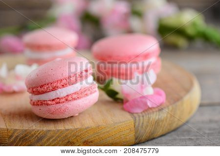 French cakes macaroons. Light pink round macaroons and flowers on a wooden board. Vintage wooden background. Sweets photo. Closeup