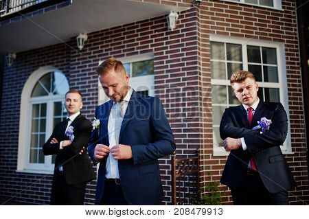 Handsome Groom In His Wedding Tuxedo Posing With Groomsmen Or Best Men Outdoor With Brick House On T